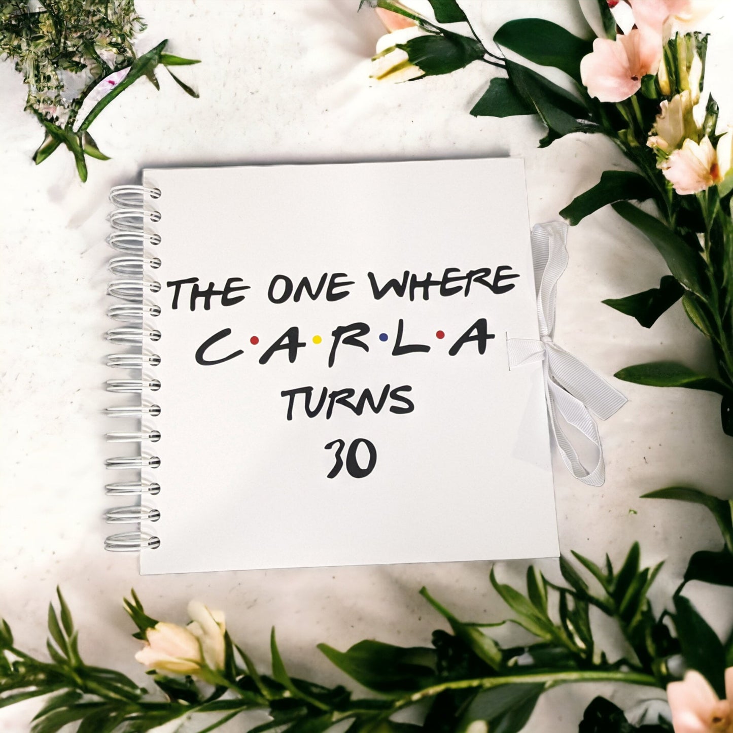 A white photo album with blank pages that says The one where Carla turns 30. With the classic friends theme