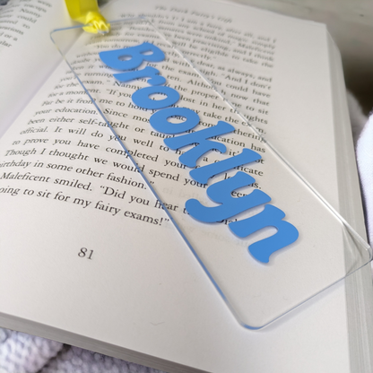 A clear name bookmark rested on an open book. The customised name is in a lovely blue colour. 