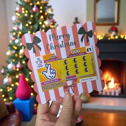 Person holding a Christmas-themed scratch card in front of a decorated Christmas tree and fireplace.