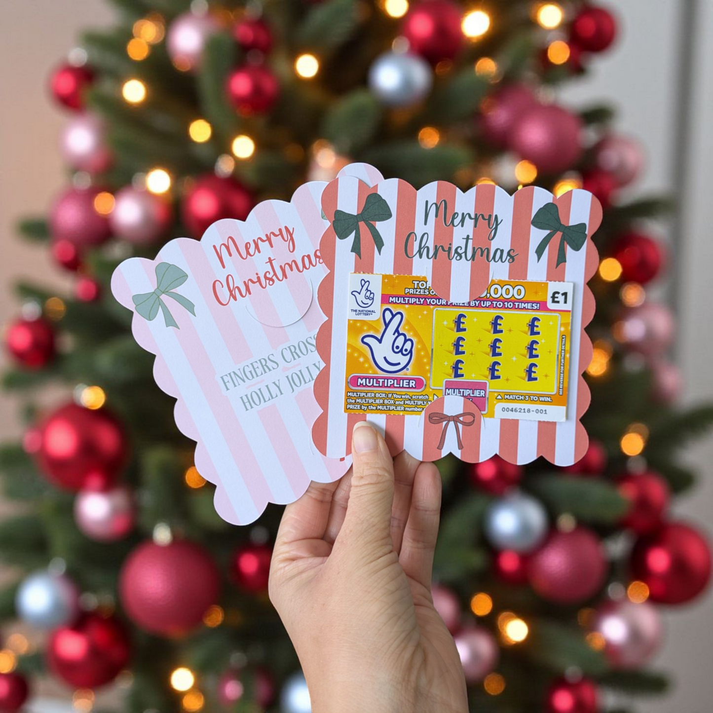 Hand holding Christmasscratch card holders with a decorated Christmas tree in the background