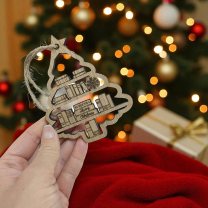Hand holding a book themed Christmas ornament with a blurred Christmas tree and presents in the background