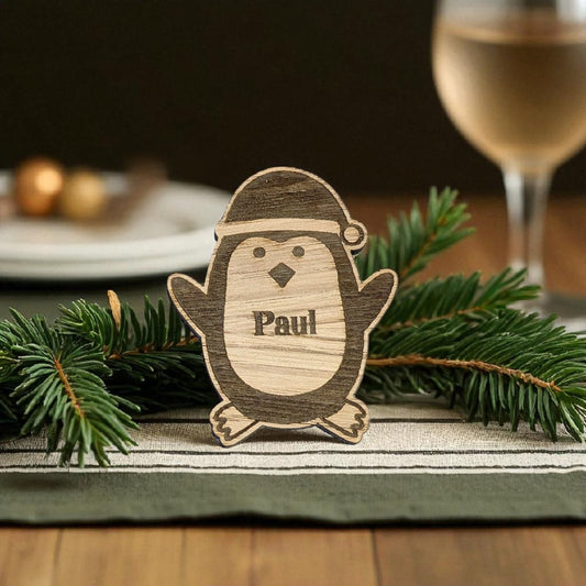 Wooden penguin chrsitmas table favour 'Paul' on a table with Christmas decorations and a glass of wine.