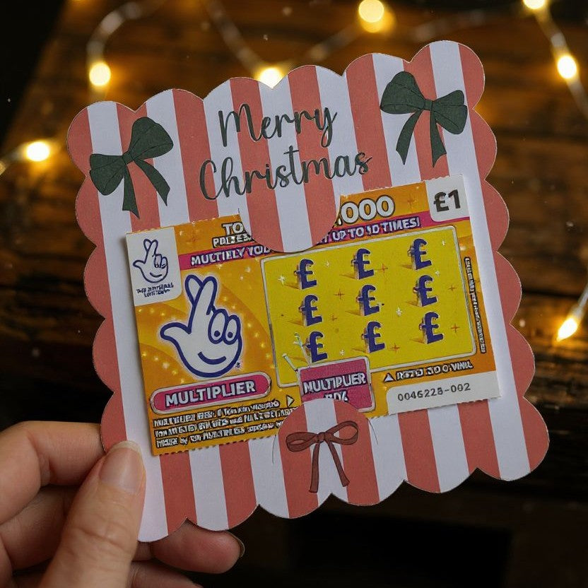 hand holding a red stripped bow 'Merry Christmas' scratch card holder held by a hand against a blurred background.