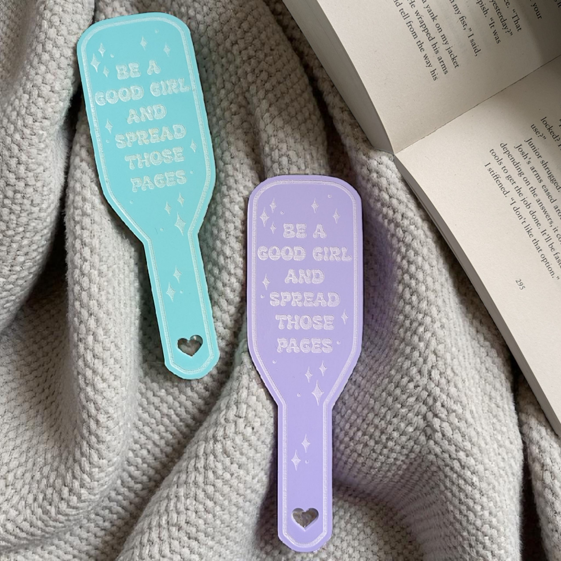 Two colorful smut bookmarks with be a good girl spread those pages text on a textured fabric background.
