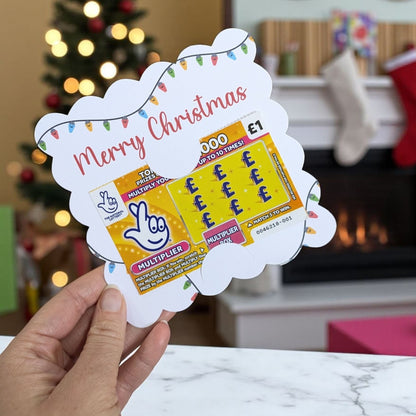 Hand holding a festive scratch card holder for stocking stuffers with Christmas decorations in the background