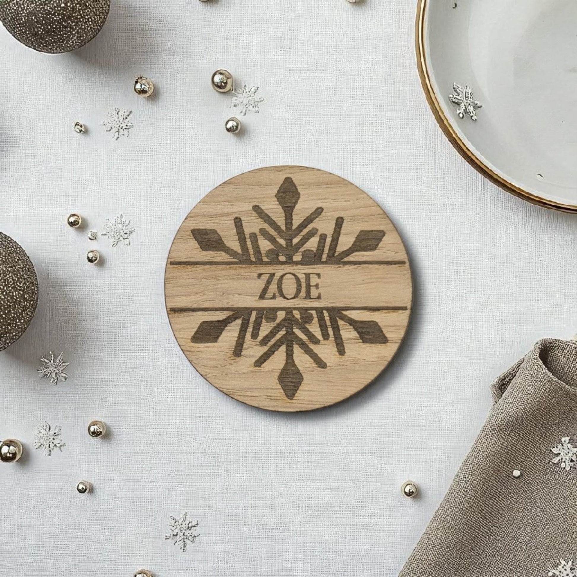 Wooden christmas name place setting with 'ZOE' engraving on a decorative surface with snowflake ornaments.