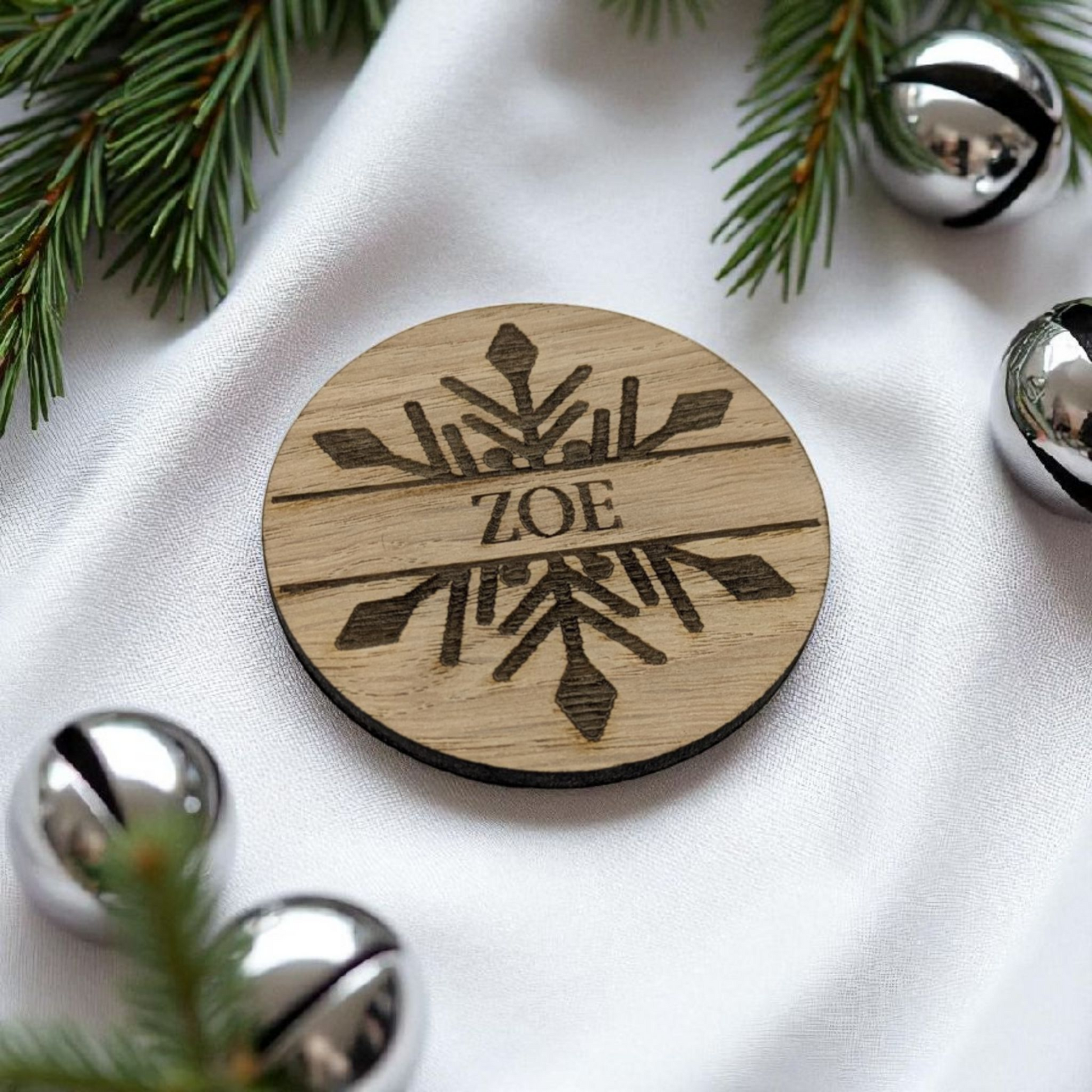 Wooden christmas table gifts with 'ZOE' engraved, surrounded by Christmas decorations on a white fabric background.