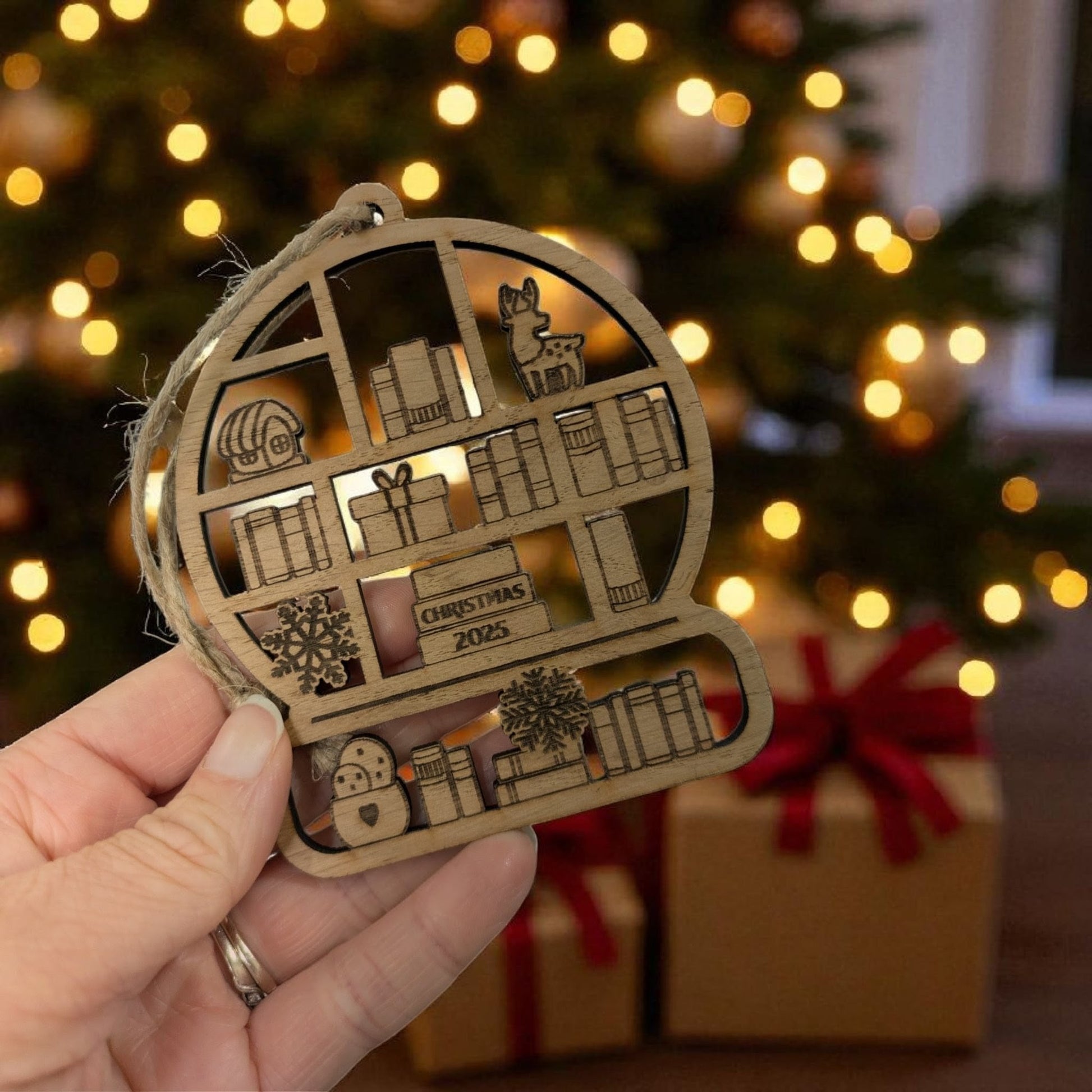 Decorative library Christmas ornament with cut-out designs held in front of a festive background with lights and presents.