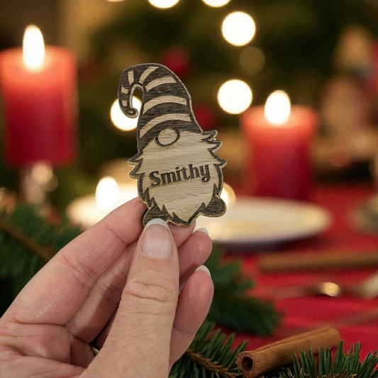 Hand holding a wooden christmas gonk table gift 'Smithy' engraved, Christmas tree and candles in the background