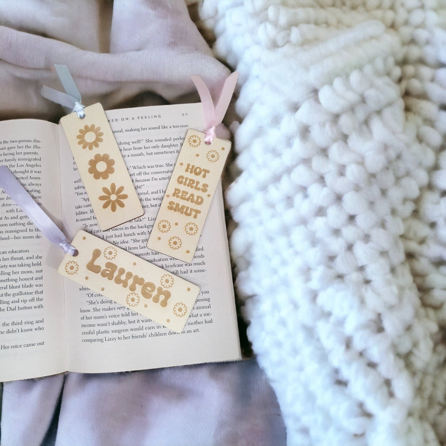 a set of three small bookmarks for adults. One reads hot girls read smut, another with 3 different daisy designs and the last with a cute floral design and a name. All details are engraved in to the wooden bookmarks.